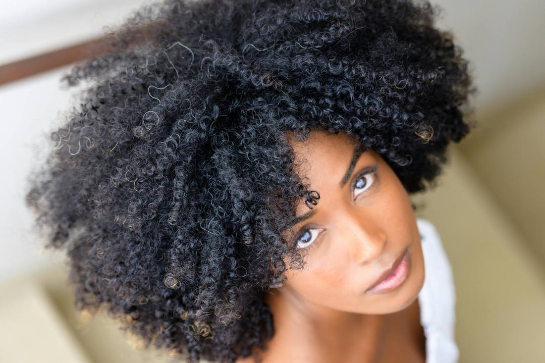 Woman with voluminous natural black curls looking upward in soft natural light