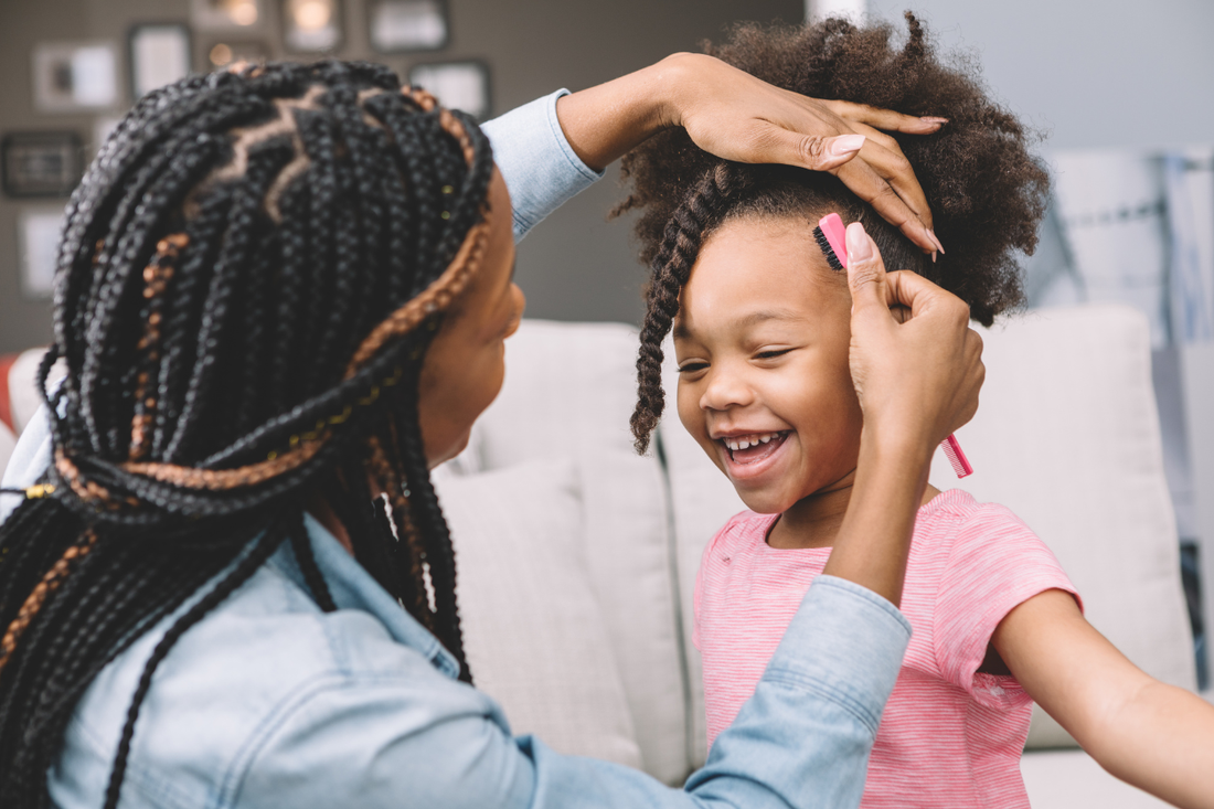 Mother styling her smiling daughter's natural hair into twists with a comb before school