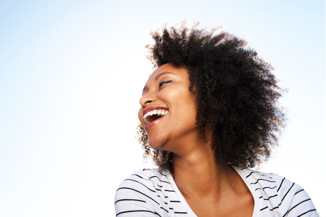 Woman with healthy, defined natural curls laughing outdoors in bright fall daylight