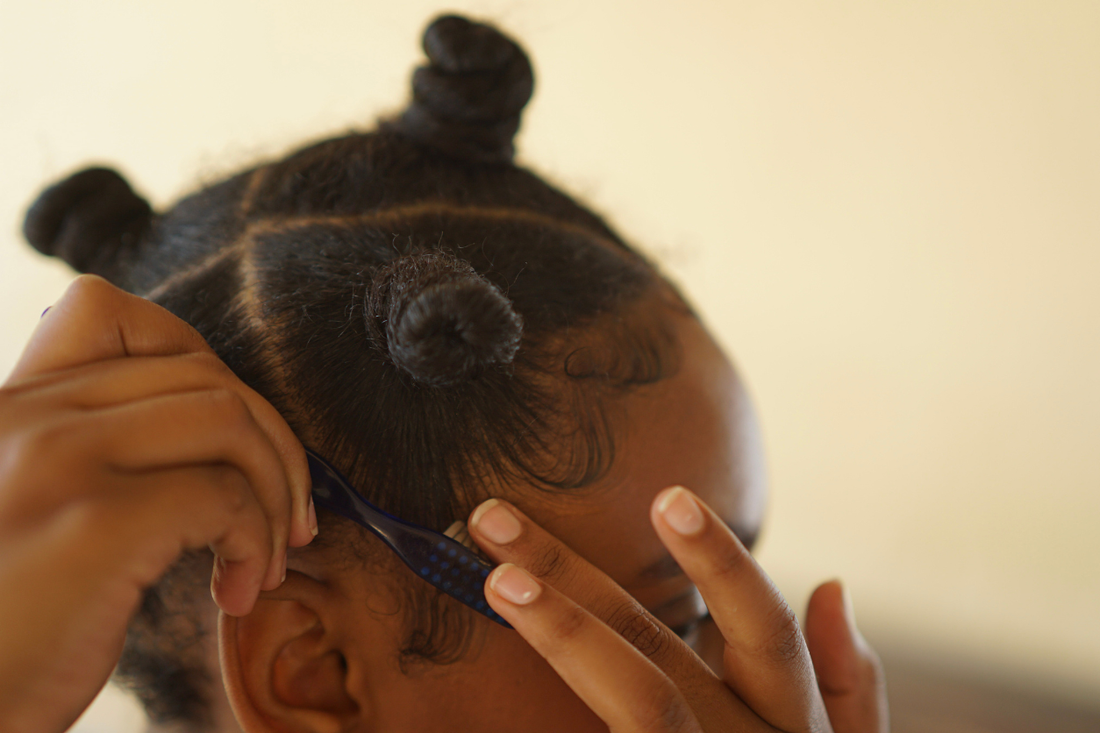 Carefully styling baby hairs with an edge brush, highlighting detail-focused hairline care.