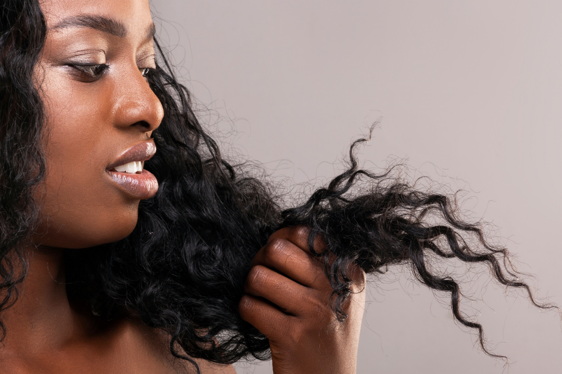 Woman examining dry, frizzy curly hair for signs of heat styling damage and breakage