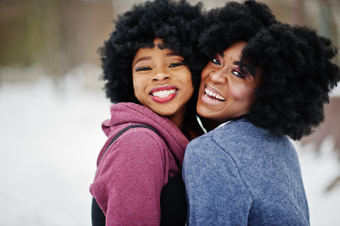 Two women with natural textured hair outdoors in winter, showing healthy curls and volume