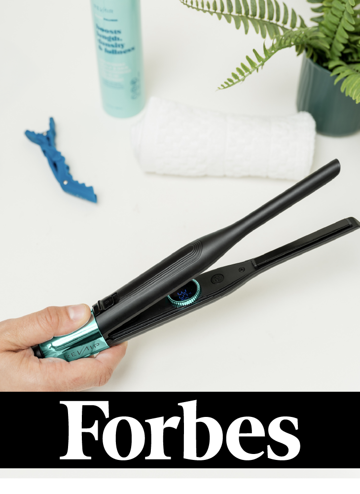 A hand holding the RevAir Micro Edge Styler flat iron next to a white towel, RevAir hair product, and potted fern on a white surface, with the Forbes logo displayed below