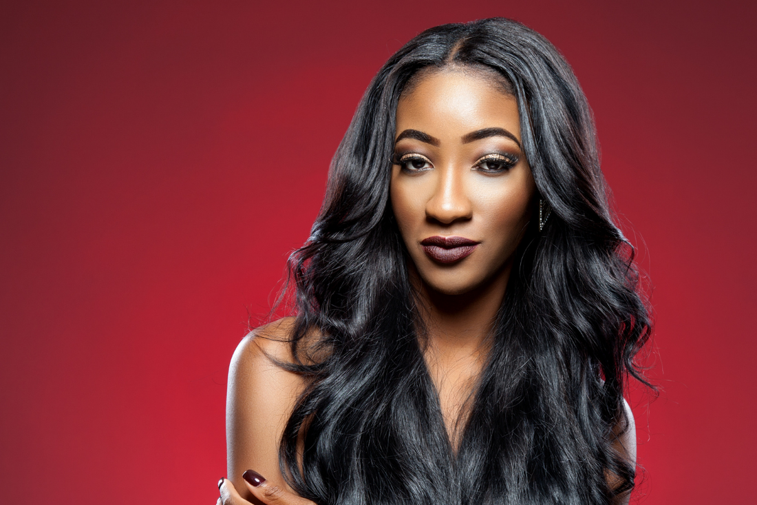 Woman with long, sleek, glossy dark hair styled in soft waves, photographed against a deep red background.