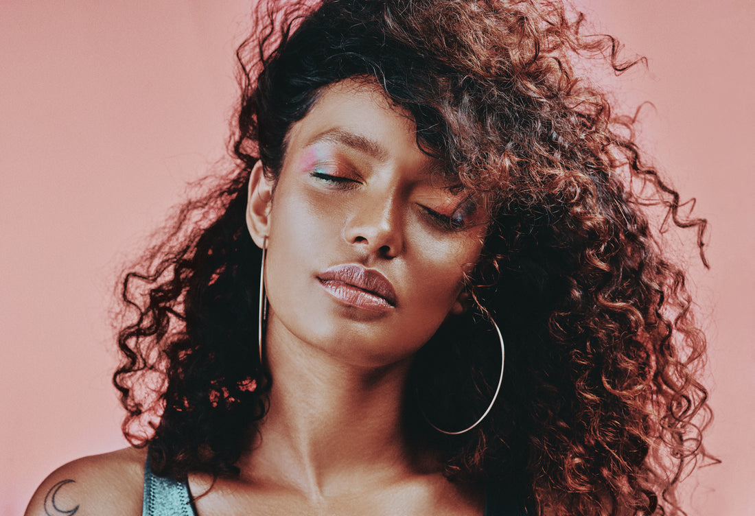 woman-with-soft-hair-curls-wearing-makeup-while-posing-against-a-pink-background-hair-hacks-concept