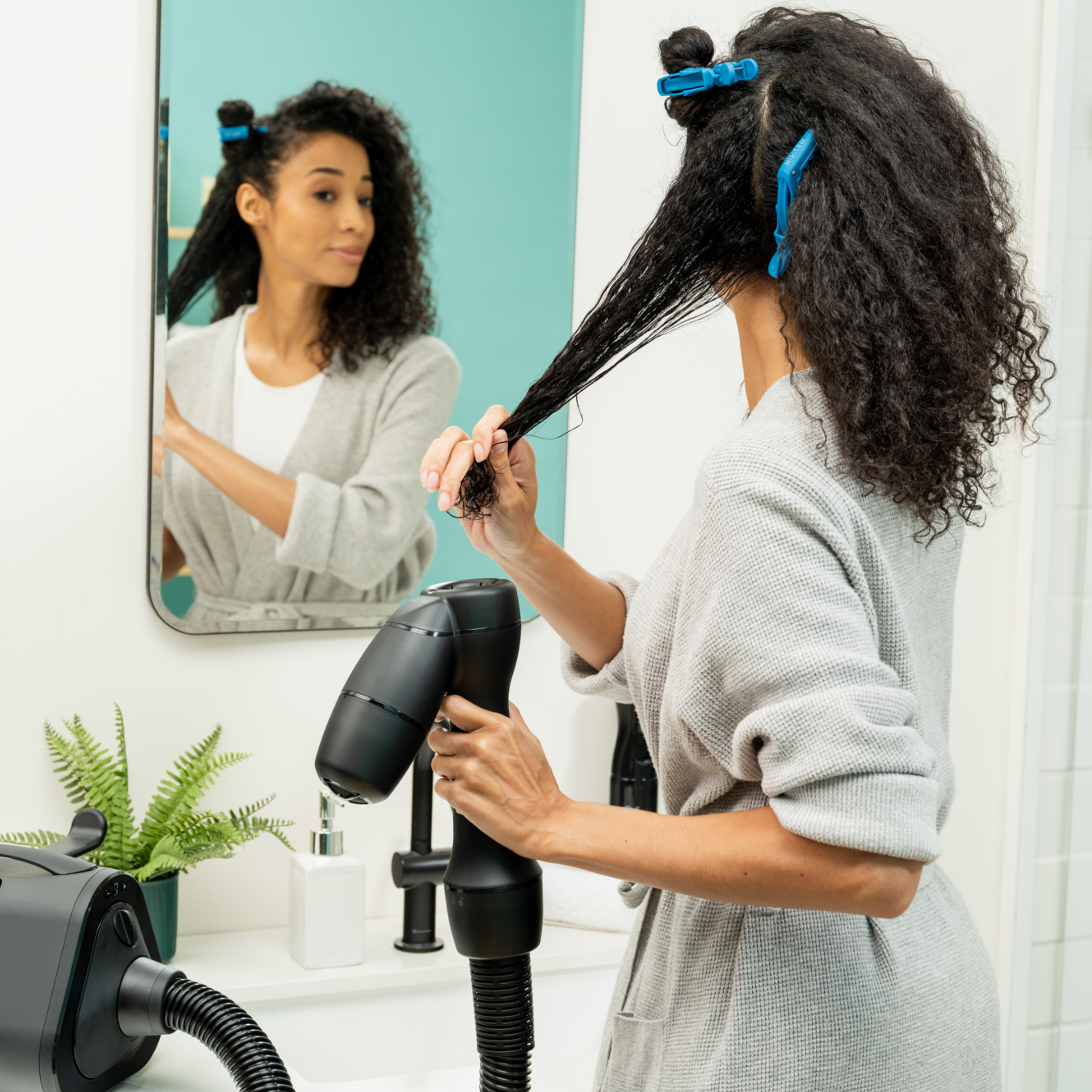 Woman in bathrobe with her curly hair sectioned with clips demonstrates placing strands of her wet hair into the RevAir dryer wand